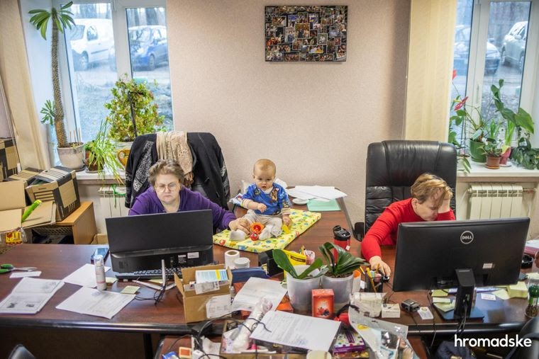 Нина Терехова держит маленькую Соломию за ногу, страхуя от падения и одновременно работая за компьютером в офисе БФ «Свои», 23 марта 2021 года