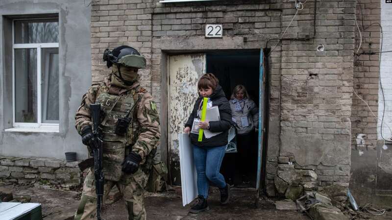 Российский военнослужащий сопровождает членов избирательного участка на так называемых выборах президента России, 17 марта 2024 года. dqxikeidqxidqrant